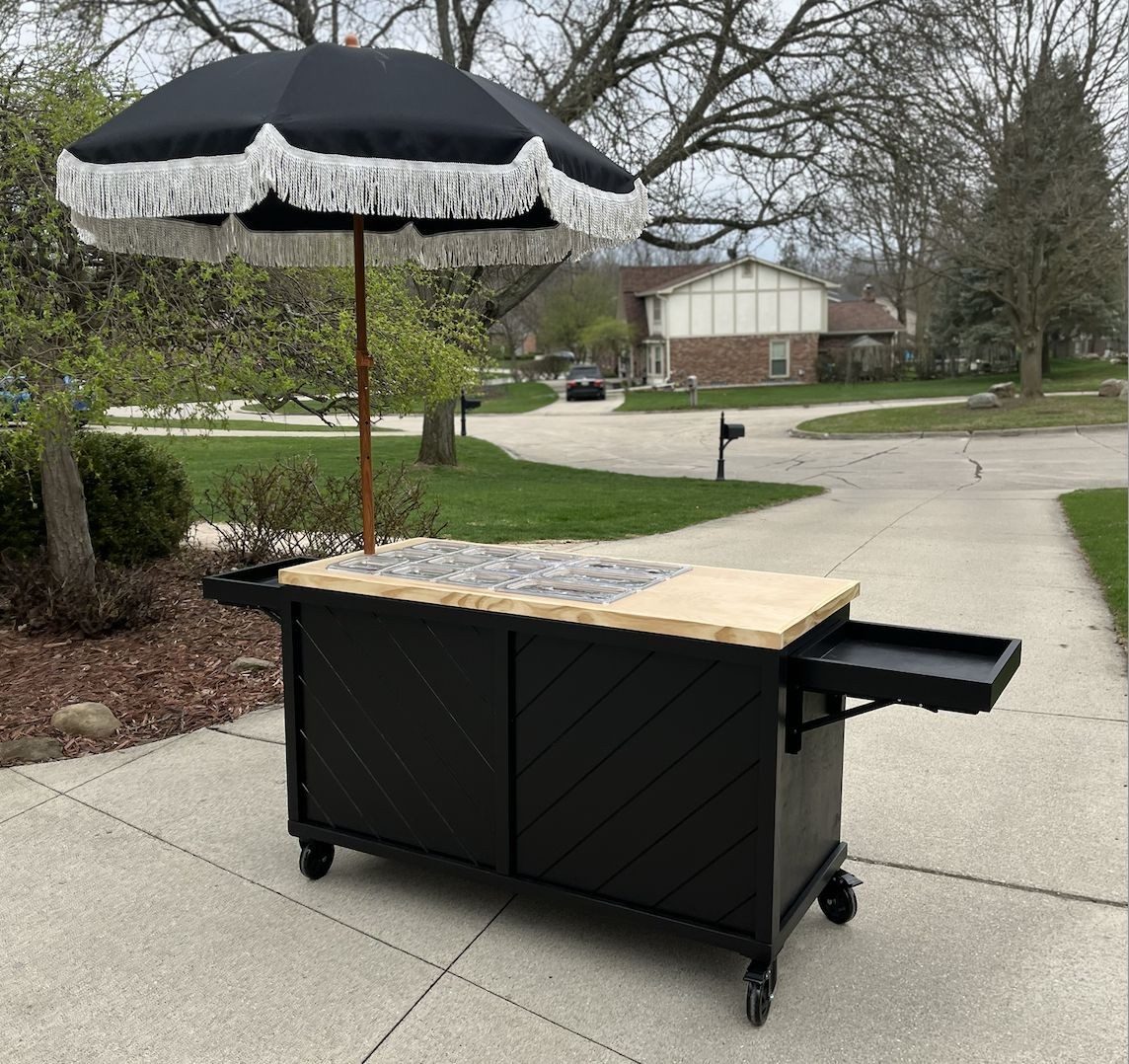 Black charcuterie and grazing cart with a chevron front, a signature wood top and a large parasol umbrella
