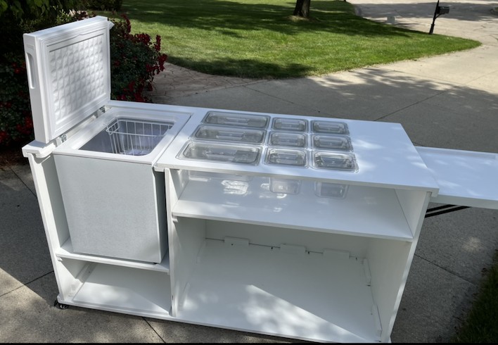 Frozen treats cart with the insulated freezer open and a full grid of acrylic wells on top