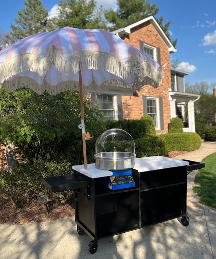 Cotton candy cart from another angle with a white top, fold-out trays and a pink-striped parasol