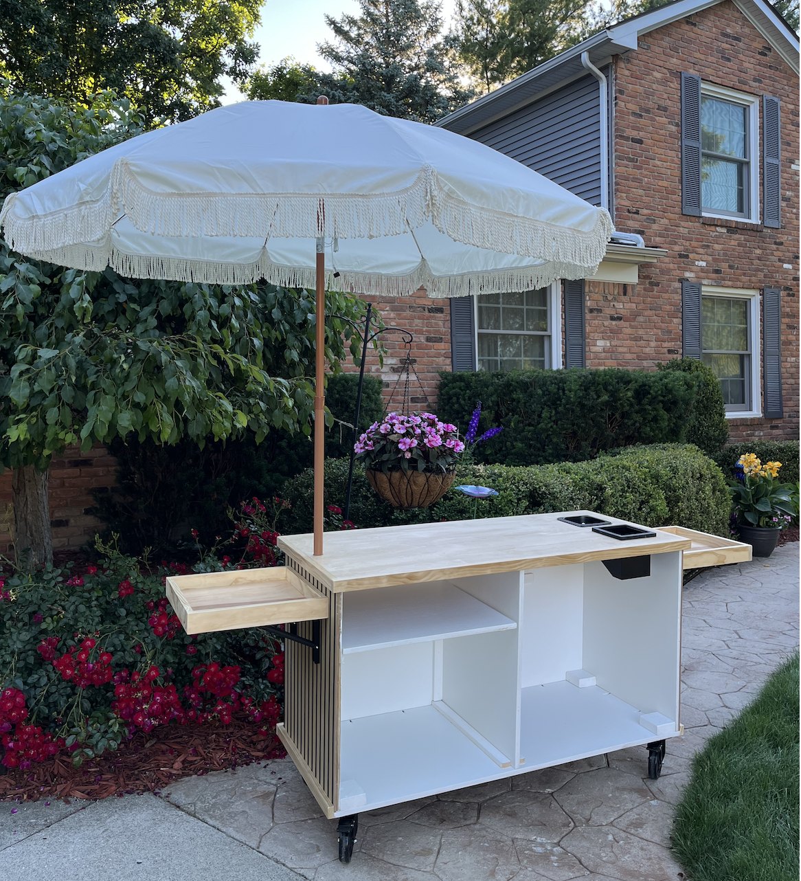 Back of the slatted-wood cart, open to show white interior storage, a fold-out natural-wood side shelf, and the wood top with a pitcher rinser and knock box