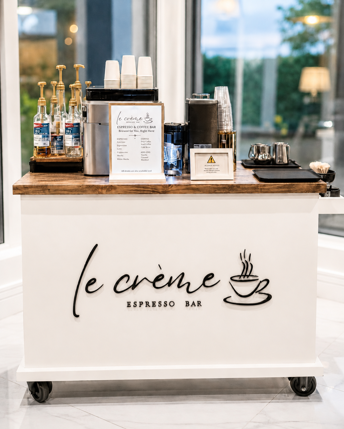 le crème Espresso Bar: a white branded coffee cart styled with an espresso machine and cups at a bright indoor event